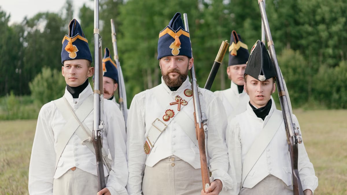Soldiers marching in historical military uniforms reenact past events outdoors.